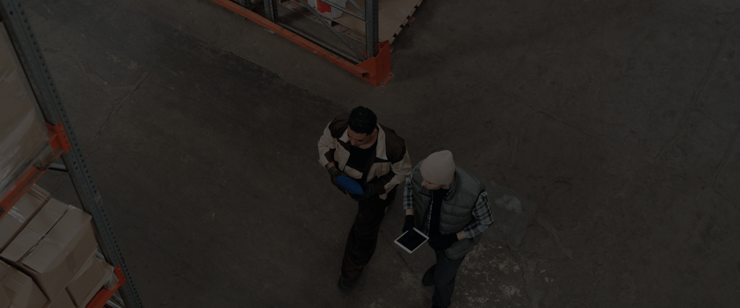 Birds-eye view of two men walking in a warehouse and one is holding a tablet