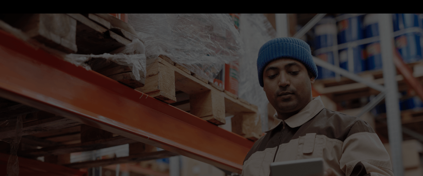 A man in a blue beanie in a warehouse looking down at his tablet