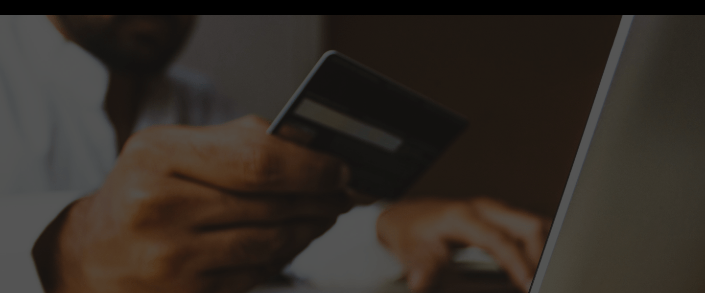 A man holding their credit card with a hand on their computer